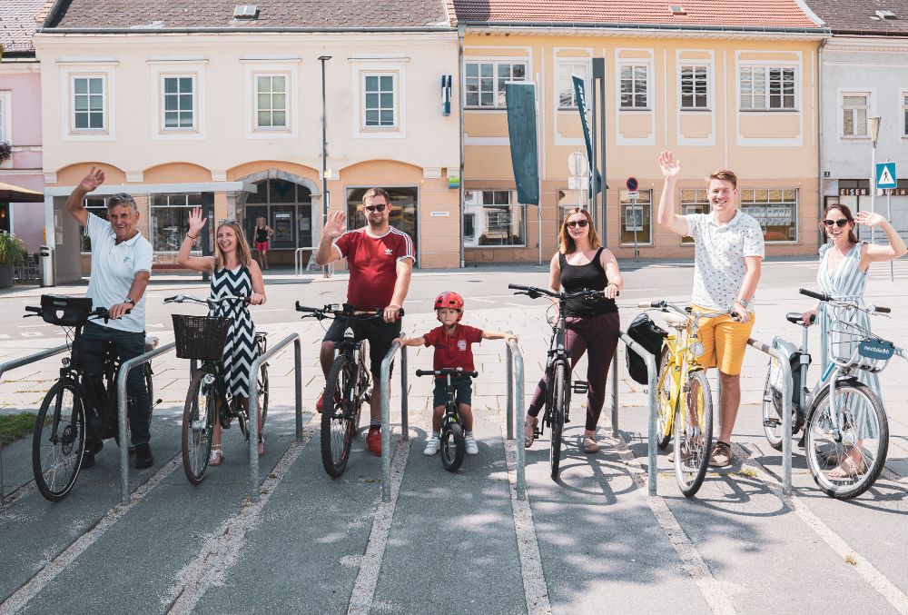 Sechs Erwachsene und ein Kind auf Fahrrädern die winken.