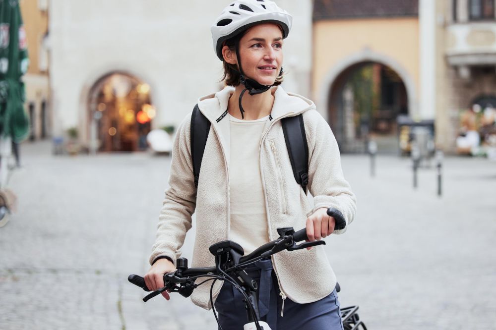 Frau mit heller Kleidung und Weste schaut weg von der Kamera und lächelt leicht